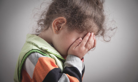 Caucasian little girl covering his face with his hands.