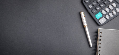 Pen, notepad and calculator on black background.
