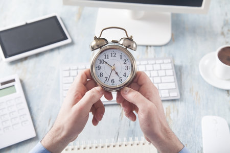Businessman sitting in the office and holding an alarm clock.