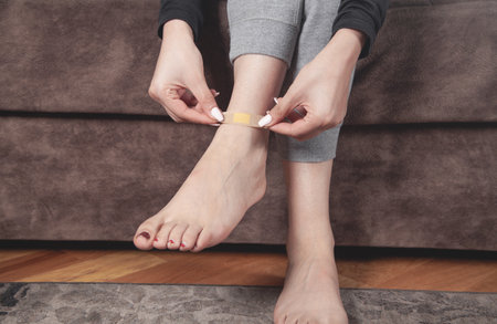 Young woman putting adhesive bandage in her leg.