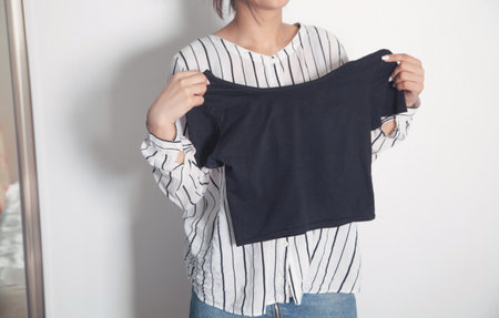 Young woman holding shirt at home.