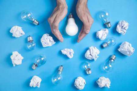 Hands protect light bulb. Crumpled papers in the blue background. ideasの写真素材