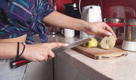 Young woman cuts fresh apple on wooden board.