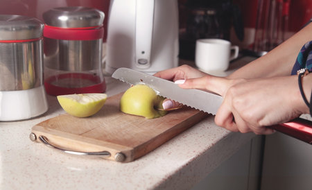 Young woman cuts fresh apple on wooden board.