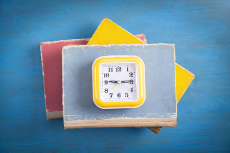 Yellow clock and books on blue wooden background.