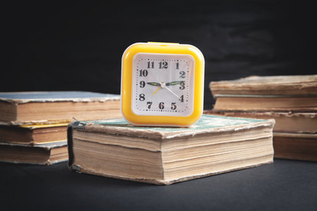 Yellow clock and books on black background.の写真素材