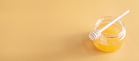 Honey jar with dipper on yellow background.