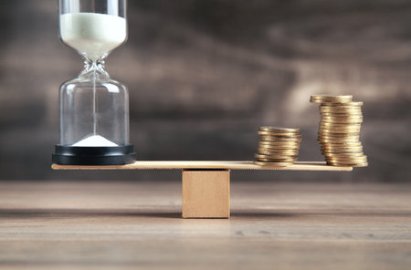 Hourglass and coins on the wooden balance.の写真素材