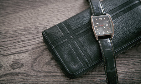 Black wristwatch and wallet on the desk.