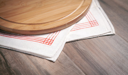 Empty pizza board and fabric tablecloth on the wooden background.