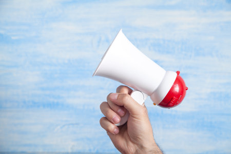 Male hand holding megaphone on blue background.