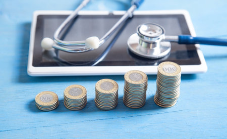 Stethoscope, tablet and coins on the blue background.