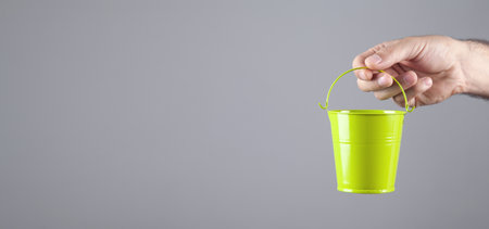 Male hand holding green metal bucket.