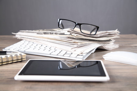 Newspapers, computer keyboard, eyeglasses on the wooden table.の写真素材
