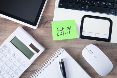 Out of office message on sticky note with computer.