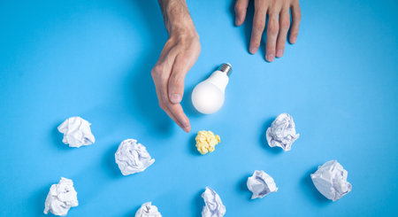Hand holding light bulb. Crumpled papers in the blue background. ideas