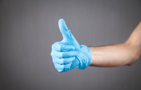 Hand in medical glove making thumb up gesture.