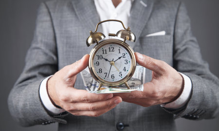 Businessman holding alarm clock and dollar banknotes.の写真素材