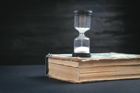 Book and hour glass on the black table.