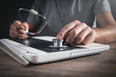 Male hand holding stethoscope on a laptop keyboard.の写真素材