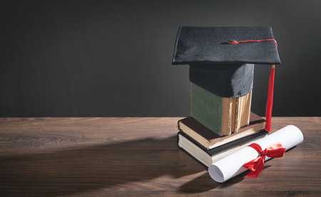 Graduation hat, book and diploma on the wooden table.の写真素材