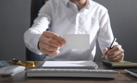 Businessman sitting in office showing white blank business card.の写真素材