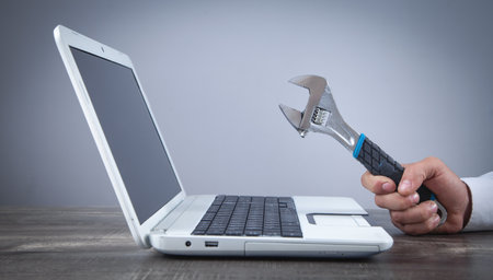 Male hand showing adjustable wrench over computer keyboard. IT service. Supportの写真素材