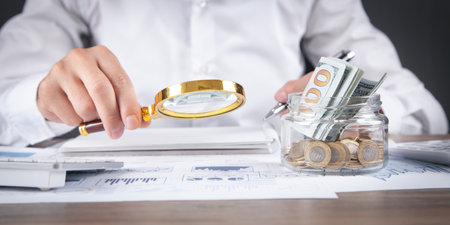 Businessman holding a magnifying glass with graphs on the desk.の写真素材