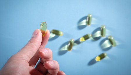 Male hand showing fish oil Omega 3 capsules on the blue background.