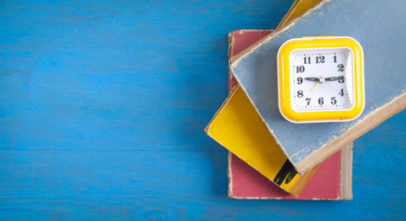 Yellow clock and books on blue wooden background.