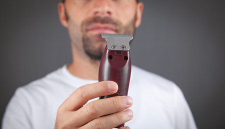 Caucasian man shaving with electric trimmer.