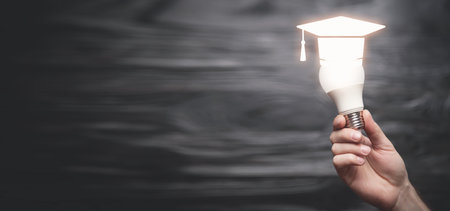 Male hand showing light bulb with a graduation cap symbol. Education