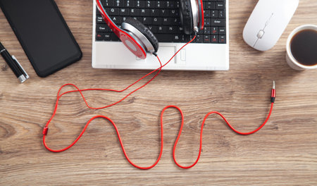 Red headphones, coffee, computer keyboard and other objects on the wooden desk.