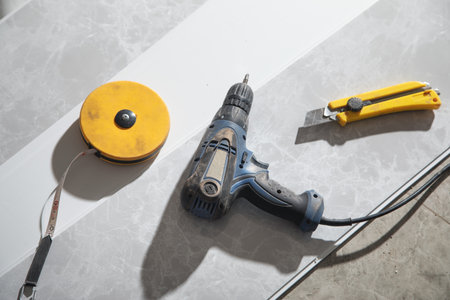 Measure tape, cutter knife, electric drill on ceiling plastic panel.