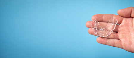 Male hand showing transparent aligner on the blue background.の写真素材