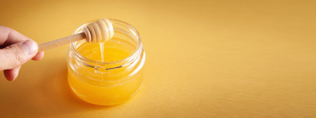 Male hand dipper and honey jar on yellow background.