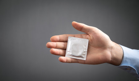 Male hand showing condom on gray background.の写真素材