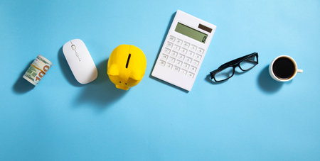 Piggy bank, money, coffee, calculator, eyeglasses on the blue background.の写真素材