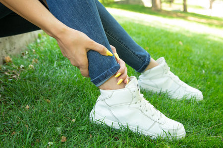 Woman suffering from ankle pain outdoors.