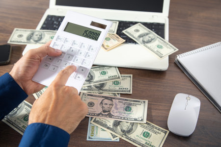 Man using calculator with a money and computer on the table.