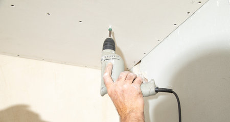 Worker with a drill screwdriver twists the screw into the drywall.の写真素材