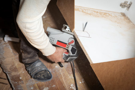 Worker cutting kitchen cabinet using electric saw.