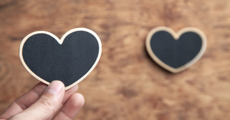 Male hand showing wooden heart on wooden table.の写真素材