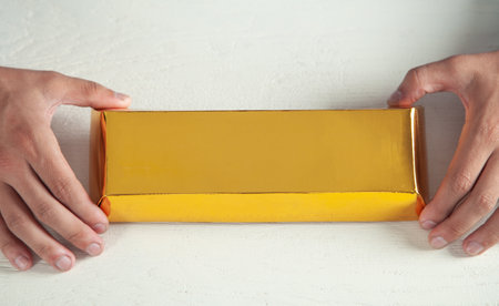 Man holding Gold bar on white desk.