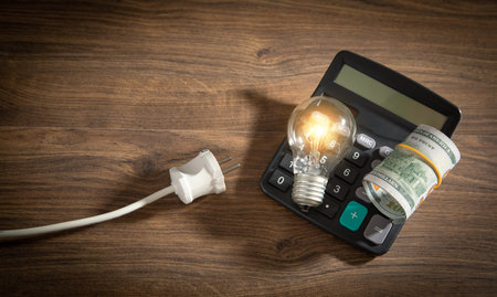 Dollar banknote, light bulb, calculator, electric plug on the wooden table. Increasing electricity...