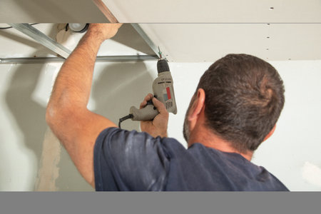 Worker with a drill screwdriver twists the screw into the drywall.の写真素材