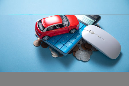 Red toy car, calculator and coins on the blue background.の写真素材