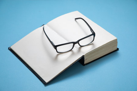 Eyeglasses and book on the blue background.