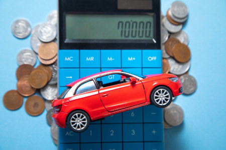 Red toy car, calculator and coins on the blue background.の写真素材