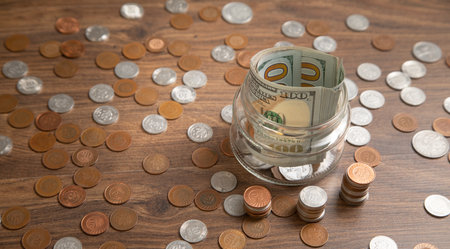 Jar of coins and dollars on wooden background.